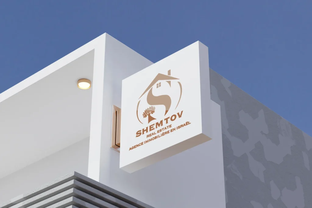 שלט חוץ מואר של Shemtov Real Estate עם לוגו בית ועץ בגוון נחושת על מבנה לבן